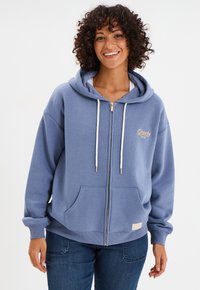 Felpa con zip azzurro chiaro realizzata in morbido tessuto, con una grande tasca frontale, cordini bianchi e logo ricamato sul lato sinistro del petto.