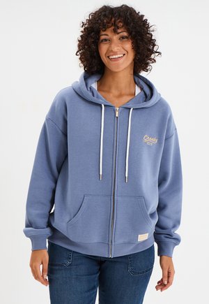 Felpa con zip azzurro chiaro realizzata in morbido tessuto, con una grande tasca frontale, cordini bianchi e logo ricamato sul lato sinistro del petto.