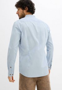 Camicia azzurra chiara a maniche lunghe con colletto classico, polsini bottonati e design a schiena dritta. Tessuto liscio, dettagli minimi.