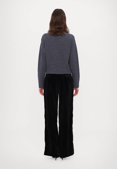 Pull gris court avec ourlet à côtes associé à un pantalon large plissé noir. Textures lisses et design minimaliste.