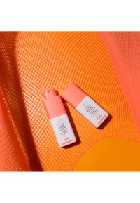 Two white cosmetic bottles with pink pumps against a textured orange background. Labels feature branding and product information.
