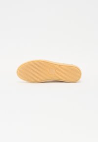 Rubber outsole with a textured, ribbed pattern; rectangular logo in the center. Light tan color, designed for grip and durability.