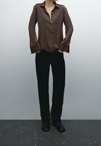 Brun skjorte med knapper og krave samt lange ærmer, parret med sorte bukser. Outfittet har et glat stof og en afslappet pasform.
