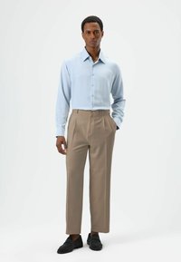 Light blue long-sleeve shirt with button closure, paired with tan pleated trousers and black slip-on shoes. Smooth fabric, tailored fit.