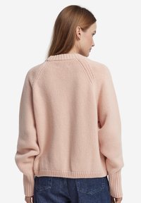 Ljusrosa stickad tröja med ribbad halsringning och mudd vid ärmslut. Har en avslappnad passform och raglanärmar, texturerat tyg och en kort design.