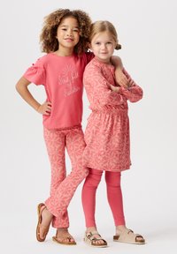 Roze t-shirt met korte mouwen met de tekst "Soul Full of Sunshine", gecombineerd met een patroonlegging en een bloemenjurk. Beide dragen sandalen.