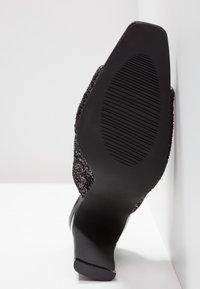 Chaussure à talon noir avec un dessus texturé, un talon lisse et une semelle en caoutchouc dotée de rainures horizontales pour une meilleure adhérence.