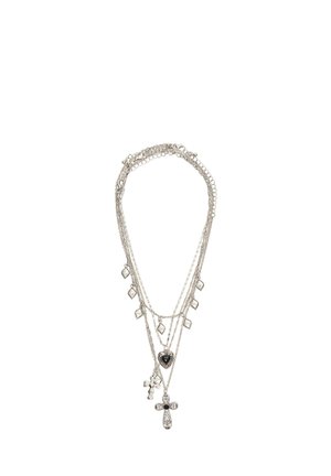 Silberne geschichtete Halskette mit mehreren Ketten, kleinen diamantförmigen Anhängern, einem Herzanhänger und zwei Kreuzanhängern vor weißem Hintergrund.