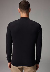 Suéter de punto negro de manga larga con cuello redondo, que presenta puños y dobladillo acanalados, textura suave y diseño ajustado.