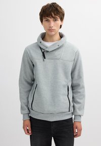 Sudadera con capucha de color gris claro, hecha de tela suave, que presenta un cierre de medio zip, cremalleras laterales y un diseño de cuello estructurado.