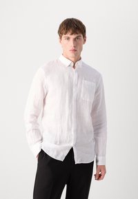Camisa branca de linho de botão com um bolso no peito, mangas compridas e um colarinho clássico, apresentando um tecido texturizado e ligeiramente transparente.