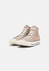 Baskets montantes en toile beige clair avec des lacets blancs, un embout en caoutchouc et des détails de semelle intermédiaire rayés.