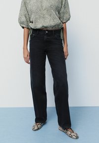Blusa verde con estampado y mangas abullonadas, combinada con jeans rectos de color azul oscuro y zapatos planos con estampado de serpiente. Tela suave y ajuste relajado.