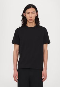 Svart crewneck t-skjorte med korte ermer, laget av mykt stoff. Har en liten, diskré logo på brystet. Minimalistisk design.
