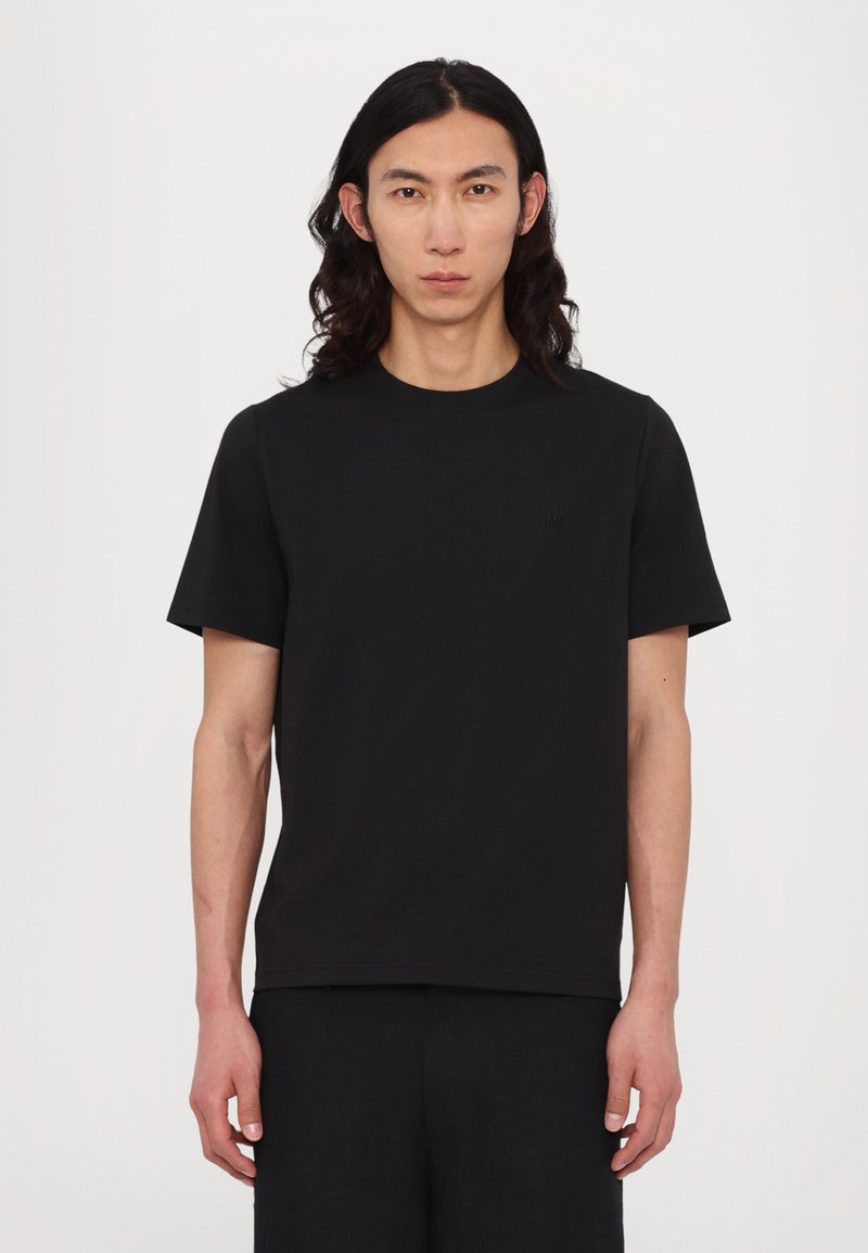Svart crewneck t-skjorte med korte ermer, laget av mykt stoff. Har en liten, diskré logo på brystet. Minimalistisk design.
