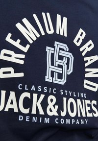 Tamnoplava pamučna majica s podebljanim bijelim tekstom: "PREMIUM BRAND," "CLASSIC STYLING," "JACK & JONES," i "DENIM COMPANY."