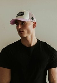 Fehér elülső panellel, rózsaszín napellenzővel �és hálós oldalakkal rendelkező baseball sapka. Elöl logó folt található. Fekete pólóval viselve.