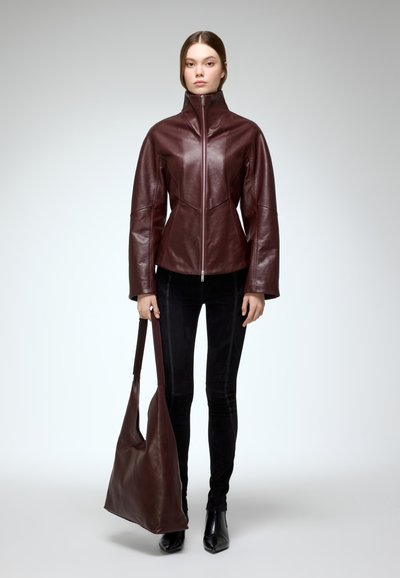 Bordeaux leren jas met een hoge kraag en ritssluiting, gecombineerd met een bijpassende leren tas en zwarte skinny broek. Gladde textuur.
