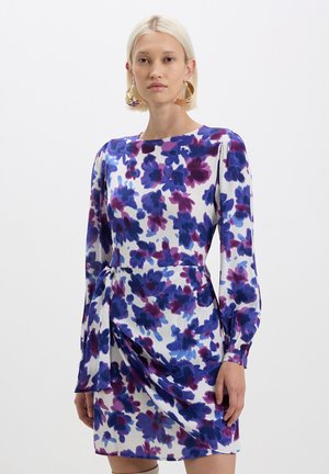 Abito a stampa floreale bianco, caratterizzato da fiori viola e blu. Maniche lunghe, scollo rotondo e un design drappeggiato con dettaglio di nodo laterale.