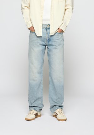 Light blue denim jeans with a relaxed fit, featuring traditional five-pocket styling and subtle fading. Worn with a cream button-up shirt and sneakers.