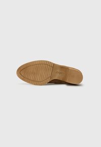 Semelle de chaussure en cuir suédé brun avec une surface en caoutchouc texturée, présentant des rainures horizontales et verticales pour plus d'adhérence. Logo en relief sur le talon.