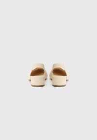 Beige Mule mit Absatz, glatter Textur, offenem Rücken und perforiertem Design am Obermaterial. Niedriger Blockabsatz und abgerundete Spitze für einen lässigen Look.