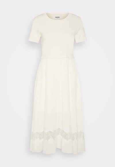 Robe blanche avec un haut en coton ajusté et une jupe fluide et transparente. L'ourlet présente des détails en dentelle complexes, créant un effet superposé.