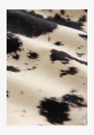 Koornekangas, millel on koorevärvi alus ja ebaregulaarsed mustad laigud; sile tekstuur vähese sädelusega, rõhutades mustrite kontrasti.