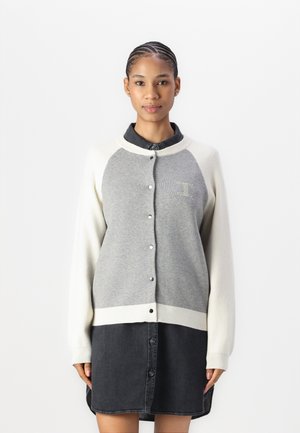 Grå cardigan med kremfargede ermer, knappelukking og ribbestrikkede mansjetter. Har en horisontal splittedesign og brodert logo på brystet.