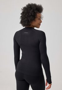 Langarm zwart sportshirt met een slim-fit ontwerp, gladde textuur en duimopeningen bij de mouwen. Bevat een discreet logo op de achterkant.