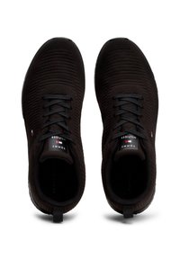 Paire de baskets en tissu tricoté noir avec des lacets noirs et le logo Tommy Hilfiger sur la languette, vue de dessus.