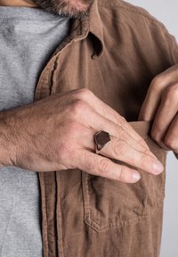 Hexagon ring met een houten inleg, zilveren metalen band. Draagt aan een hand nabij een bruine corduroy shirt. Huidtextuur zichtbaar.