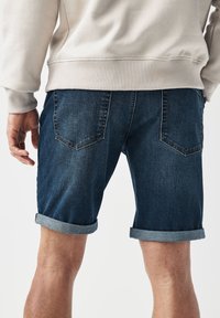 Jeansshorts, blau mit einem ausgewaschenen Finish, haben umgeschlagene Säume, zwei Gesäßtaschen und kontrastierende Nähte. Das Material ist weich und dennoch strapazierfähig.