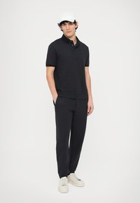 Černé tričko s límečkem a texturovaným vzorem s krátkými rukávy, doplněné o kalhoty ve stejném stylu. Dokončeno bílými teniskami a bílou čepicí.