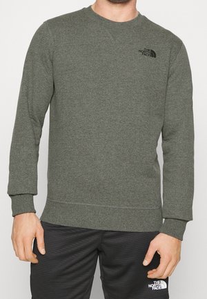 Mężczyzna w oliwkowozielonej, długorękawowej bluzie i czarnych spodniach, oba z logo The North Face na klatce piersiowej i udzie.