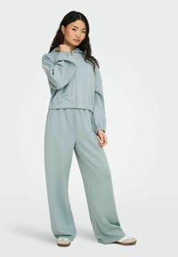 Lys blå, zip-up hettegenser med en avslappet passform og elastiske mansjetter, kombinert med matchende vide bukser. Myk stoff med en jevn tekstur.