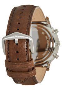 Brauner Lederarmband mit Naht und Metallschließe. Im Hintergrund ist ein silbernes Uhrengehäuse sichtbar, das eine polierte und reflektierende Oberfläche zeigt.