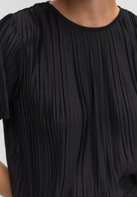 Schwarzes, plissiertes Oberteil mit rundem Halsausschnitt und kurzen Puffärmeln, das vertikale Rillen für Textur und ein glattes Stofffinish aufweist.
