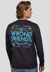 Svart sweatshirt i bomull med en stor turkos grafisk design på baksidan som visar texten "The WRONG FRIENDS Design House" i en dekorativ stil.