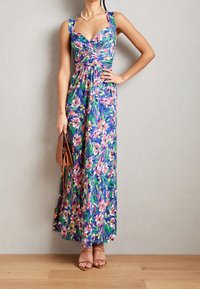 Kukallinen maksimekko syvällä V-kaula-aukolla, kierretyllä vartalolla ja leveillä olkaimilla. Elinvoimainen sininen kangas, jossa on vaaleanpunaisia ja vihreitä kukkakuoseja.