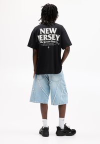 Sort bomulds T-shirt med hvid tekst "NEW JERSEY" på ryggen. Denim shorts i lyseblå farve, med let oprevet kant og kontrasterende syninger.