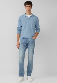 Niebieski sweter w paski z dekoltem w serek i białą podkoszulką, do tego jasnoniebieskie dżinsy i białe trampki.