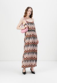 Maxi-jurk met zigzagpatroon in orange, wit en zwart; lichtgewicht stof, dunne banden, gecombineerd met een roze handtas en zwarte hakken.