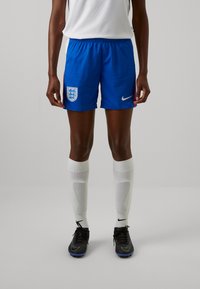 Pantalones cortos de fútbol Nike azul con el escudo de Inglaterra, presentan una cinturilla elástica. Zapatillas de fútbol negras con detalles en blanco y calcetines blancos.