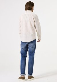 Camisa de manga larga con estampado de luces y cuello, combinada con jeans de denim azules. Zapatos de ante y puños enrollados en los tobillos.