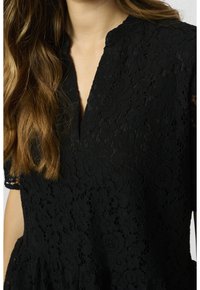 Top in pizzo nero con scollatura a V, motivo floreale, maniche corte e una texture sottile, che mette in risalto dettagli di design intricati.