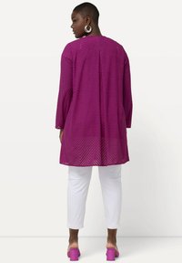 Dlouhý rukáv, tunika s fialovým chevronovým vzorem a jemnou texturou, spárovaná s bílými kalhotami a růžovými sandály na blokovém podpatku.