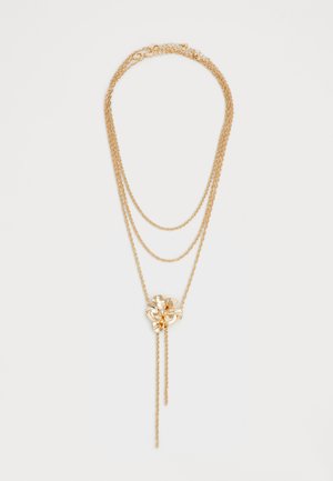 Gold layered necklace with three delicate chains and a central flower pendant featuring a small gemstone in the middle and two dangling chains.
