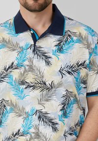 Korte mouw polo shirt met een lichtblauwe achtergrond en een palmbladpatroon in zwart, blauw en beige. Donkerblauwe kraag met turquoise accenten.