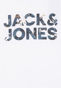 Bela bombažna majica z bold napisom "JACK & JONES", napolnjenim s cvetnim vzorcem v odtenkih zelene, modre in oranžne.